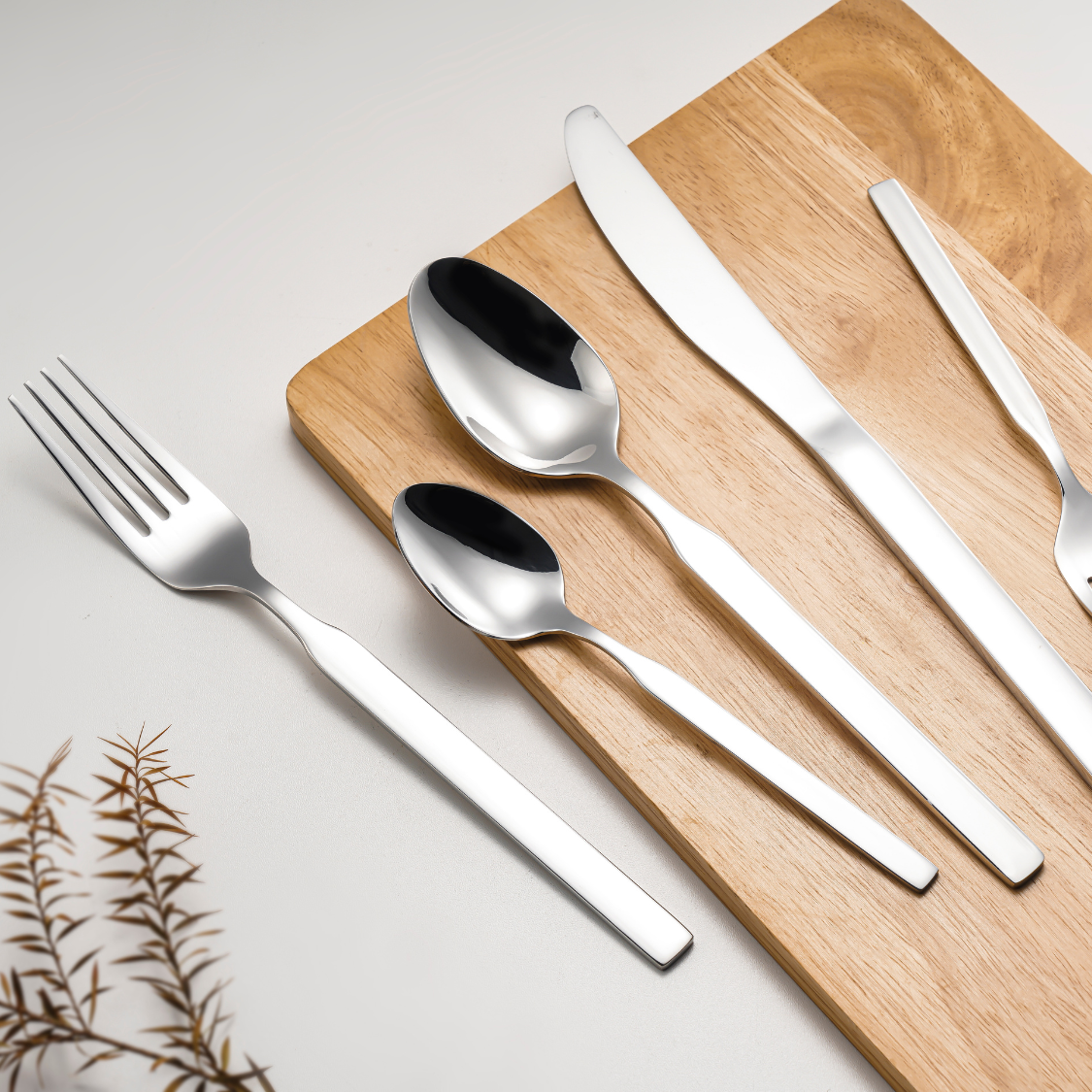 Silver cutlery set on a wooden cutting board with a light background