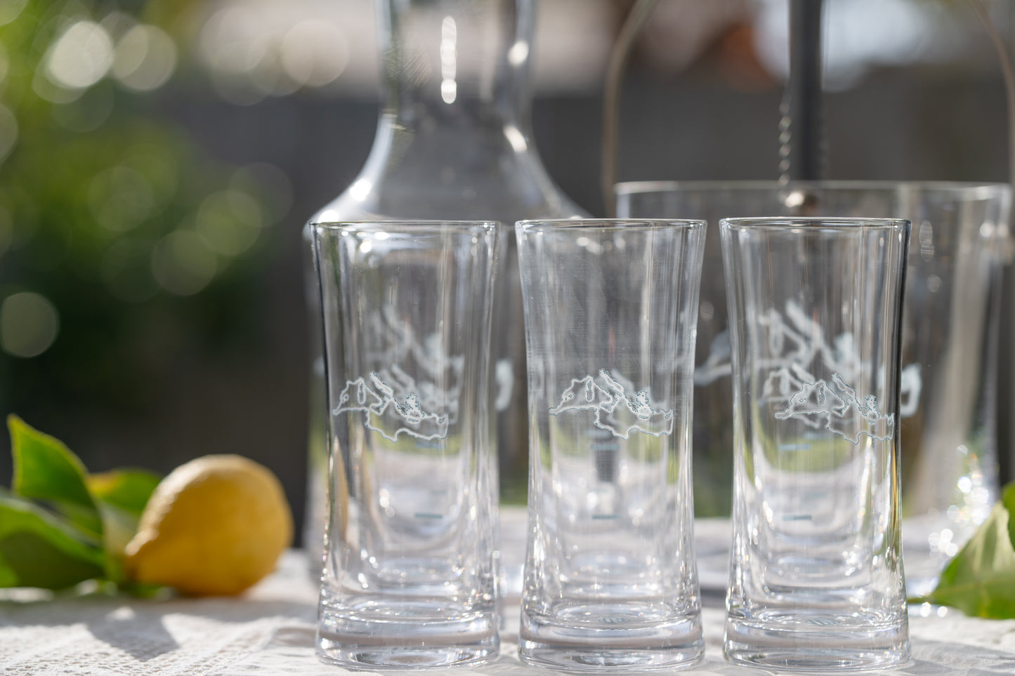 Set of three clear Ouzo glasses with engraved design on a blurred outdoor background