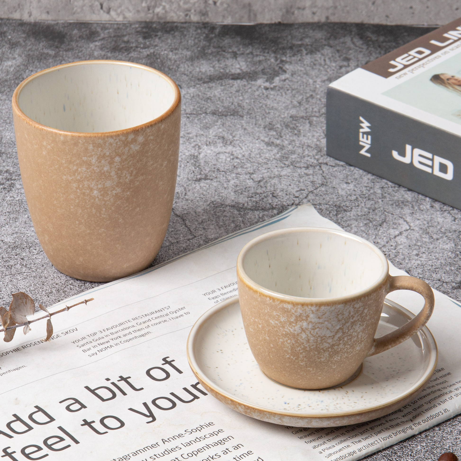 Two ceramic mugs on a newspaper with a book titled 'JED' in the background.