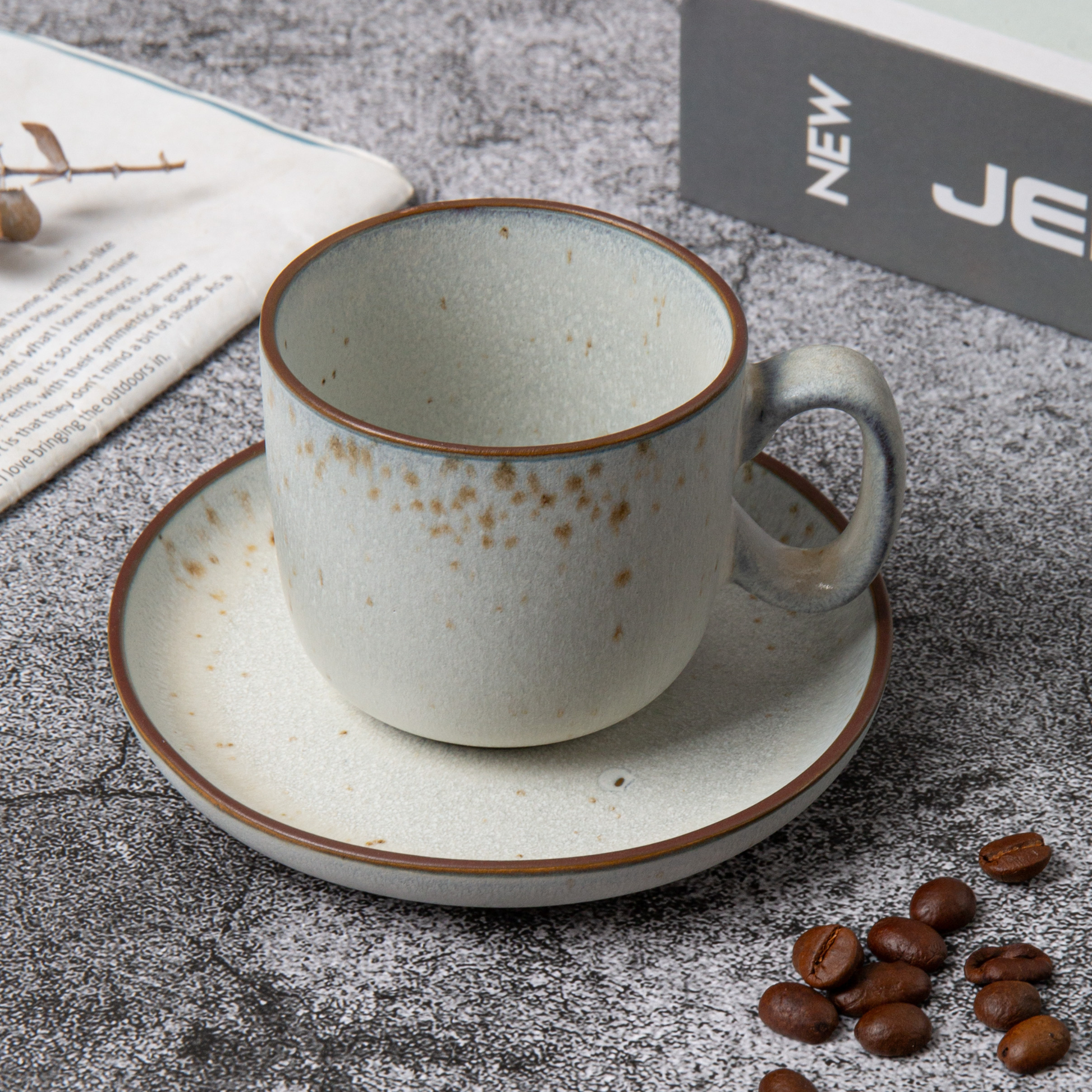 Ceramic coffee cup and saucer with coffee beans on a textured surface