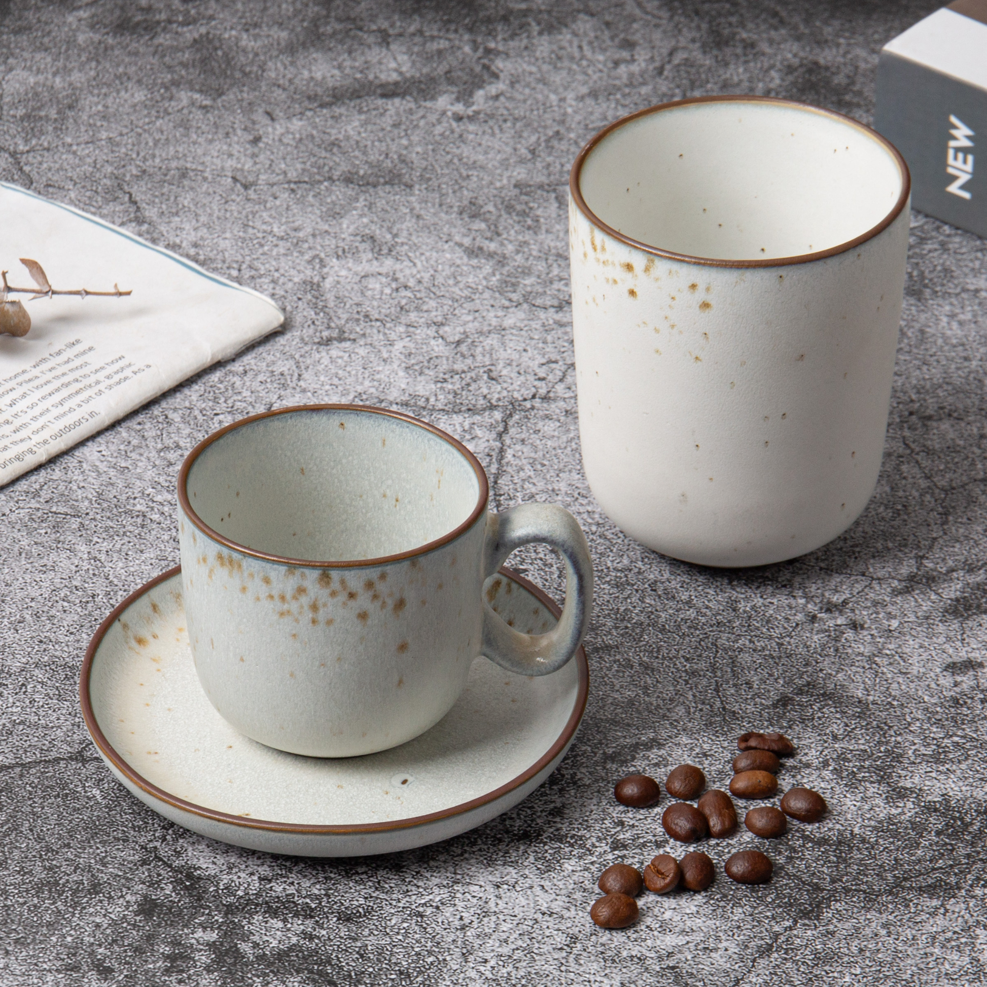 Two ceramic coffee cups with a saucer on a textured surface with coffee beans.