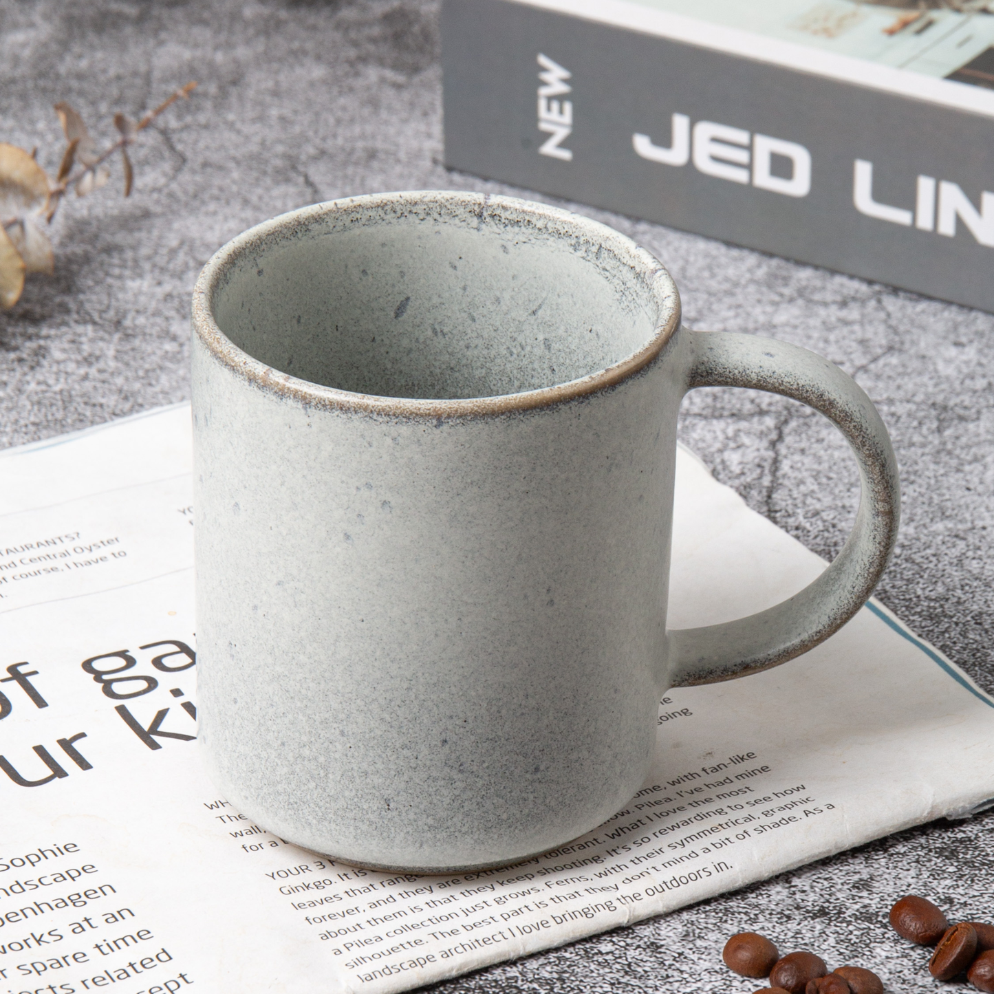 Gray ceramic mug on a newspaper with coffee beans and a magazine in the background