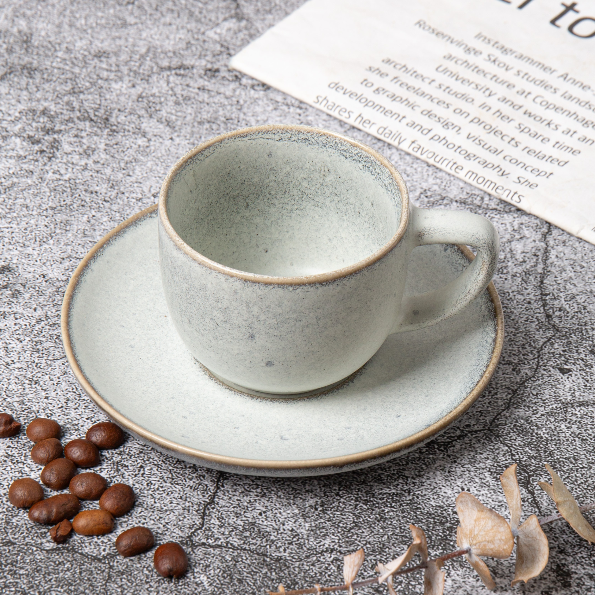 Ceramic cup and saucer with coffee beans on a textured surface