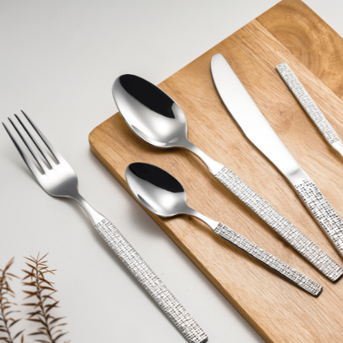 Silver cutlery set with decorative handles on a wooden board.