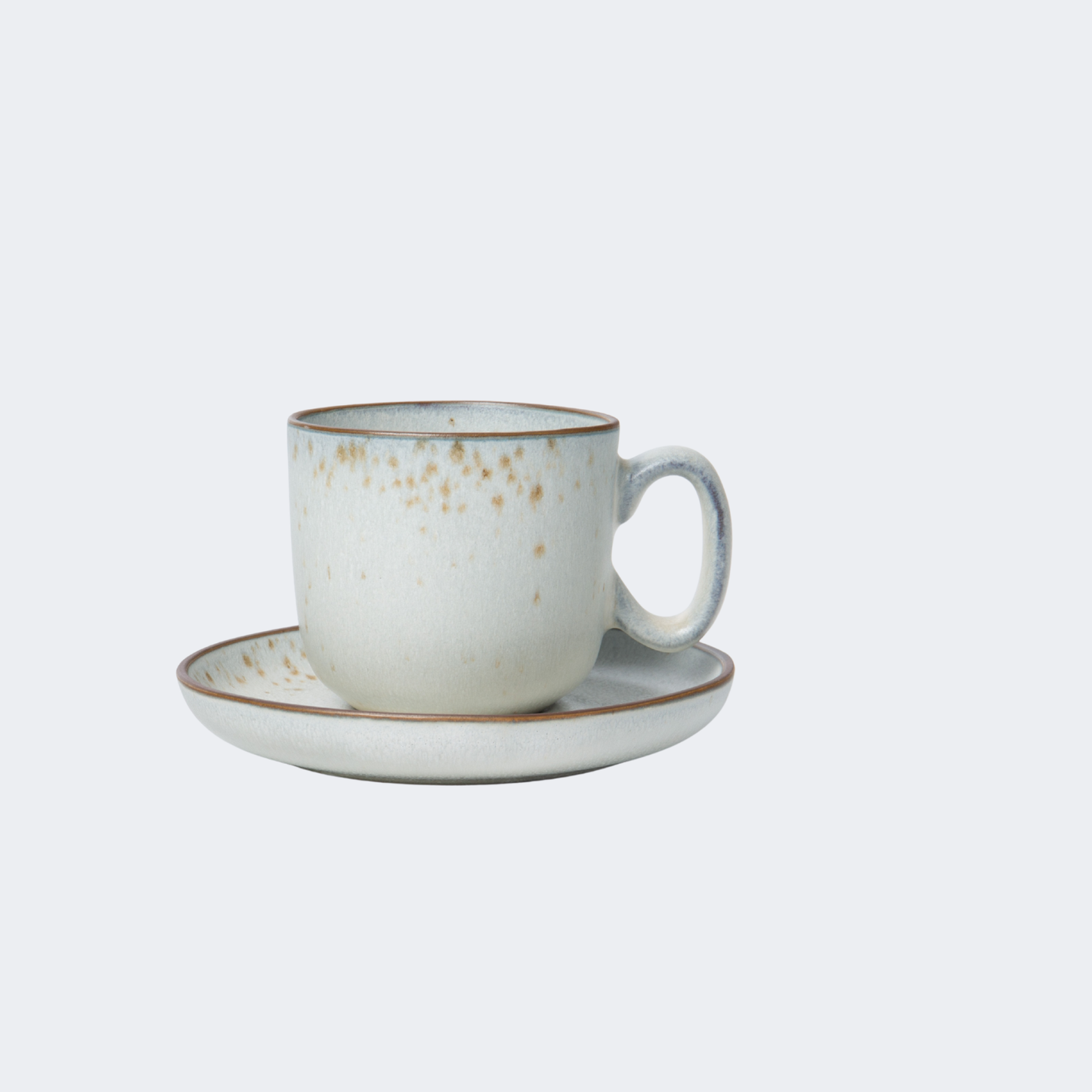 Ceramic cup with gold speckles and matching saucer on a light gray background