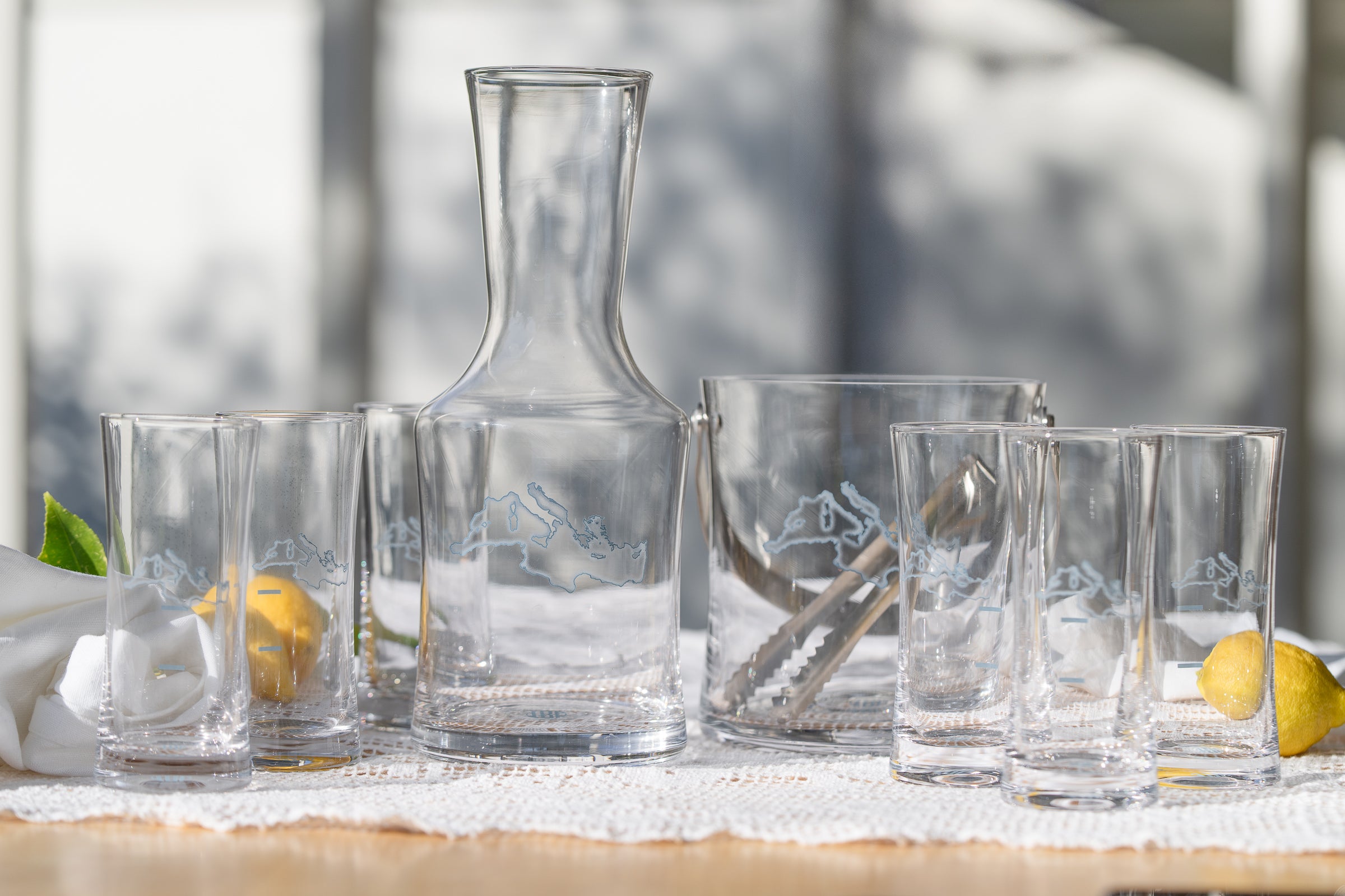 Set of clear glass tumblers and a carafe on a table with a blurred natural background