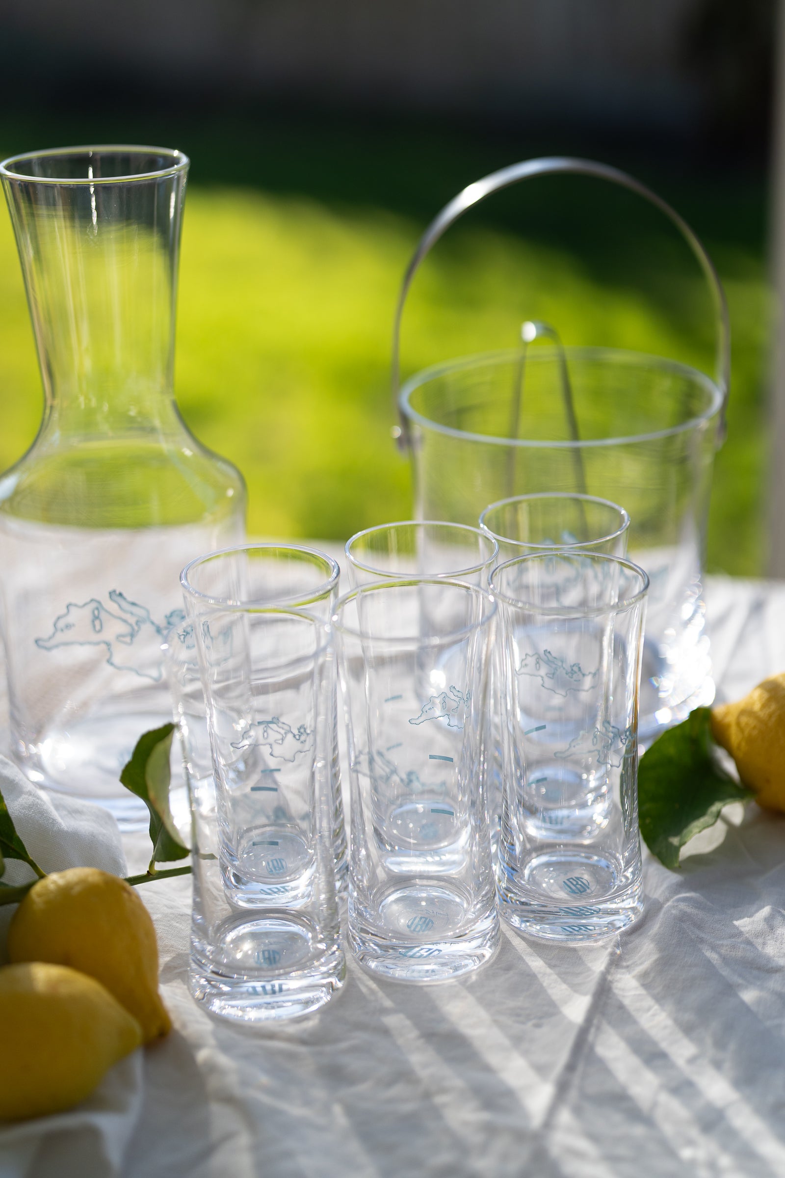 Clear glass tumblers with a carafe on a table outdoors with lemons and a bucket.